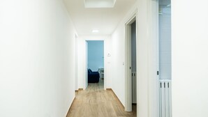 A hallway with wooden flooring, white walls, and a door leading to a room with a blue sofa. - The Flower House by Wonderful Italy (Bitritto)