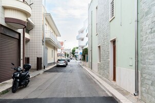 Una calle estrecha flanqueada por edificios residenciales, una motocicleta estacionada y algunos automóviles.