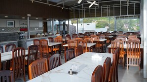 A modern restaurant with marble-topped tables and wooden chairs, a bar area, and large windows offering a view of the city. - Ketti Heights Resorts (Coonoor)