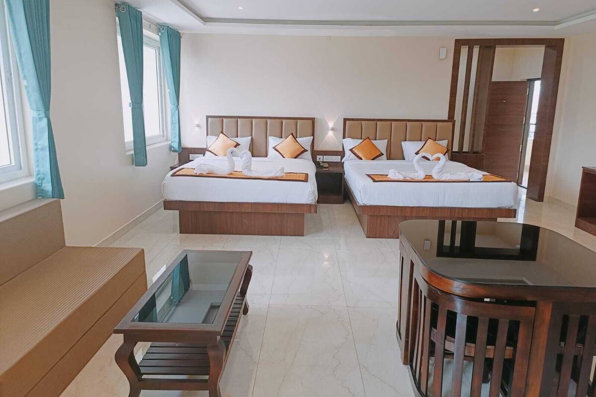 Une chambre d’hôtel avec deux lits, un banc en bois, une table avec un plateau en verre et une chaise en bois.
