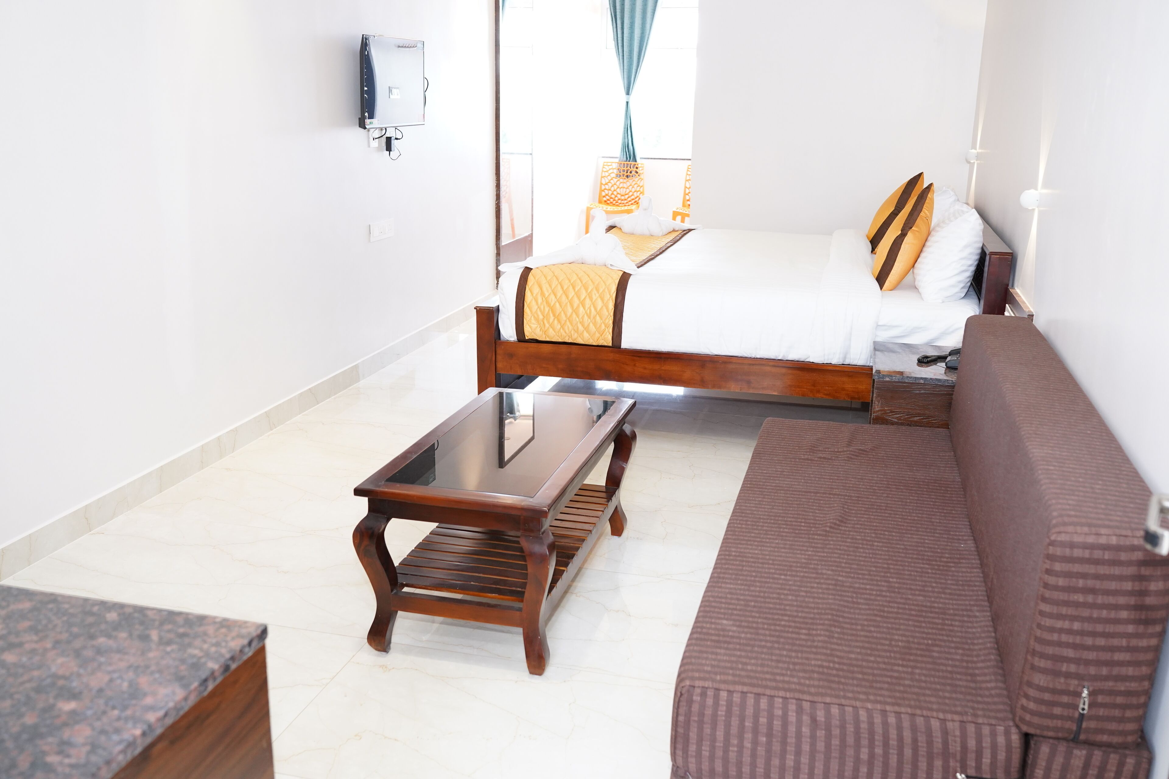 Een hotelkamer met een bed, een bruine bank, een houten salontafel en een klein bureau.