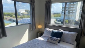 Habitación de hotel con una cama grande, una mesita de noche con lámpara y vistas a un edificio y un puente.
