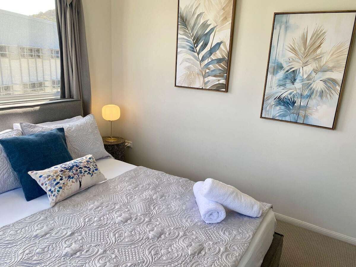 Un lit bien fait, avec une couvre-lit à motifs, une serviette enroulée et des coussins décoratifs.