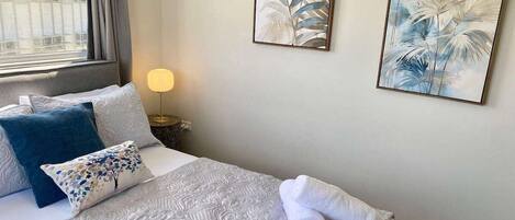 Un lit bien fait, avec une couvre-lit à motifs, une serviette enroulée et des coussins décoratifs.