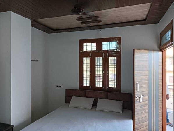 Une chambre avec un plafond en bois, un lit avec deux oreillers, une fenêtre avec un cadre en bois et une porte avec un panneau en bois.