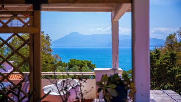 Ein überdachter Außenbereich mit Blick auf das Meer und ein Berg in der Ferne.
