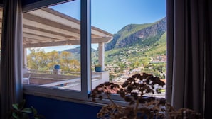 Ein Fenster mit Blick auf eine gebirgige Landschaft und ein Balkon mit einer Topfpflanze.