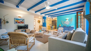 Ein Wohnzimmer mit Fernseher, Rattanmöbeln, einer blauen Akzentwand und einem Deckenventilator.