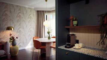 A modern living room with a round dining table, orange chairs, a sofa, a lamp, and a coffee machine on the counter.