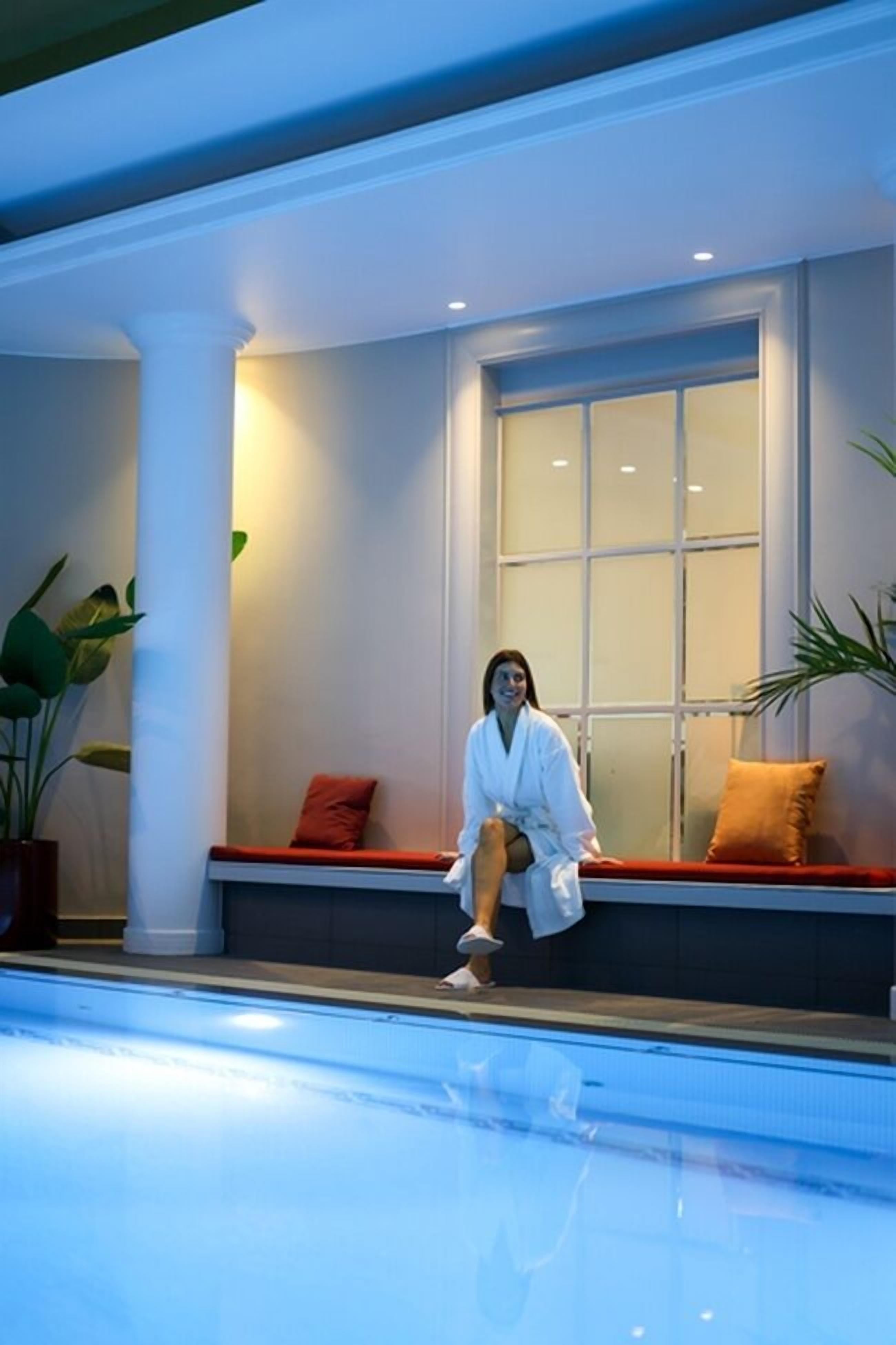 A person sitting by a poolside with a window and plants in the background.