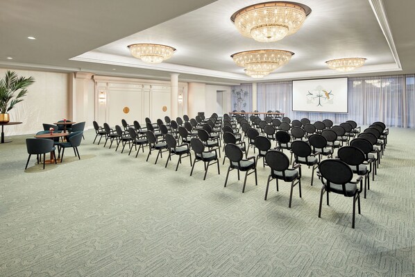A conference room with rows of chairs, a projector screen, and chandeliers. - Van der Valk Hotel Park Lane Antwerpen (Antwerp)