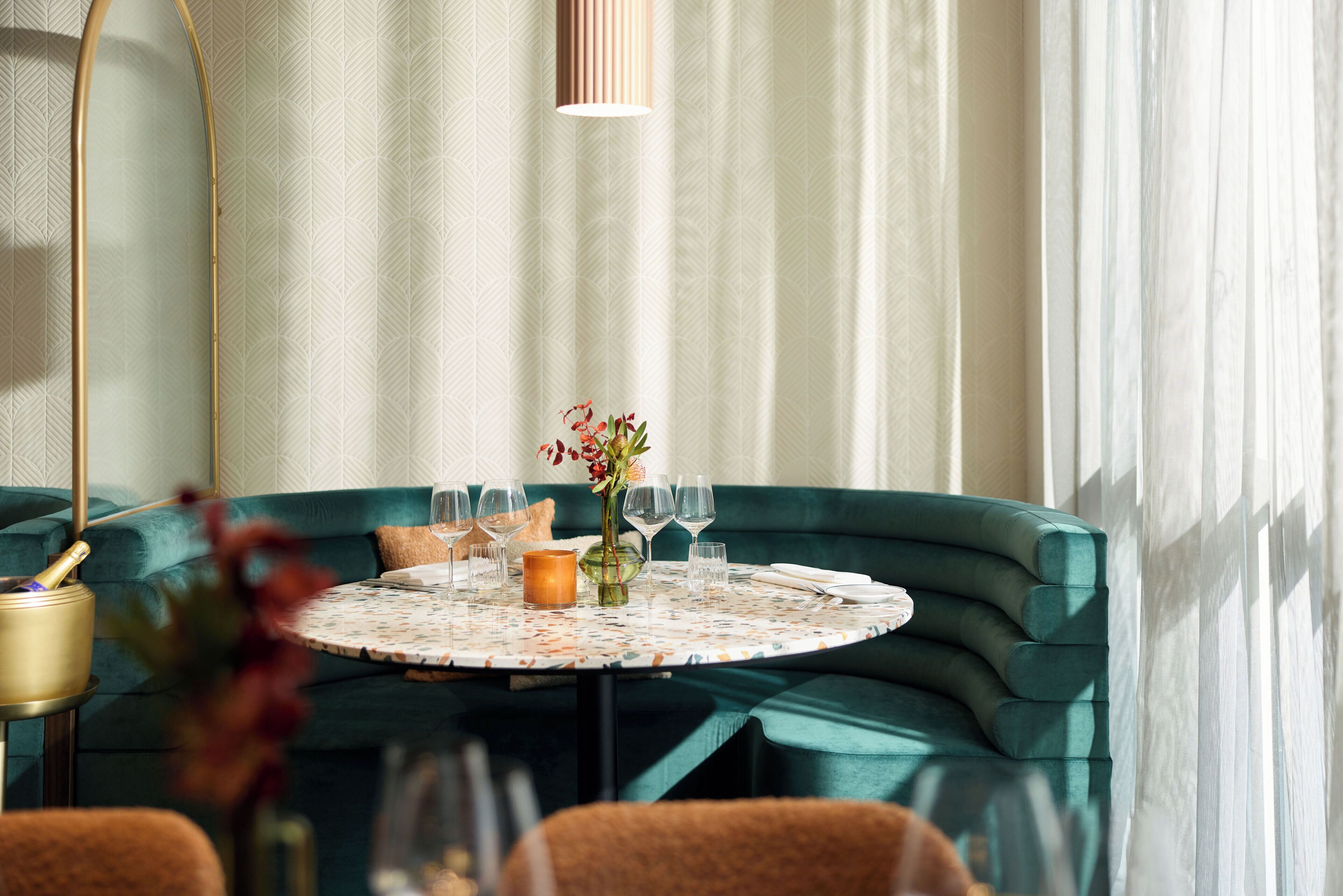 A round table with a floral tablecloth, a vase with flowers, and wine glasses.