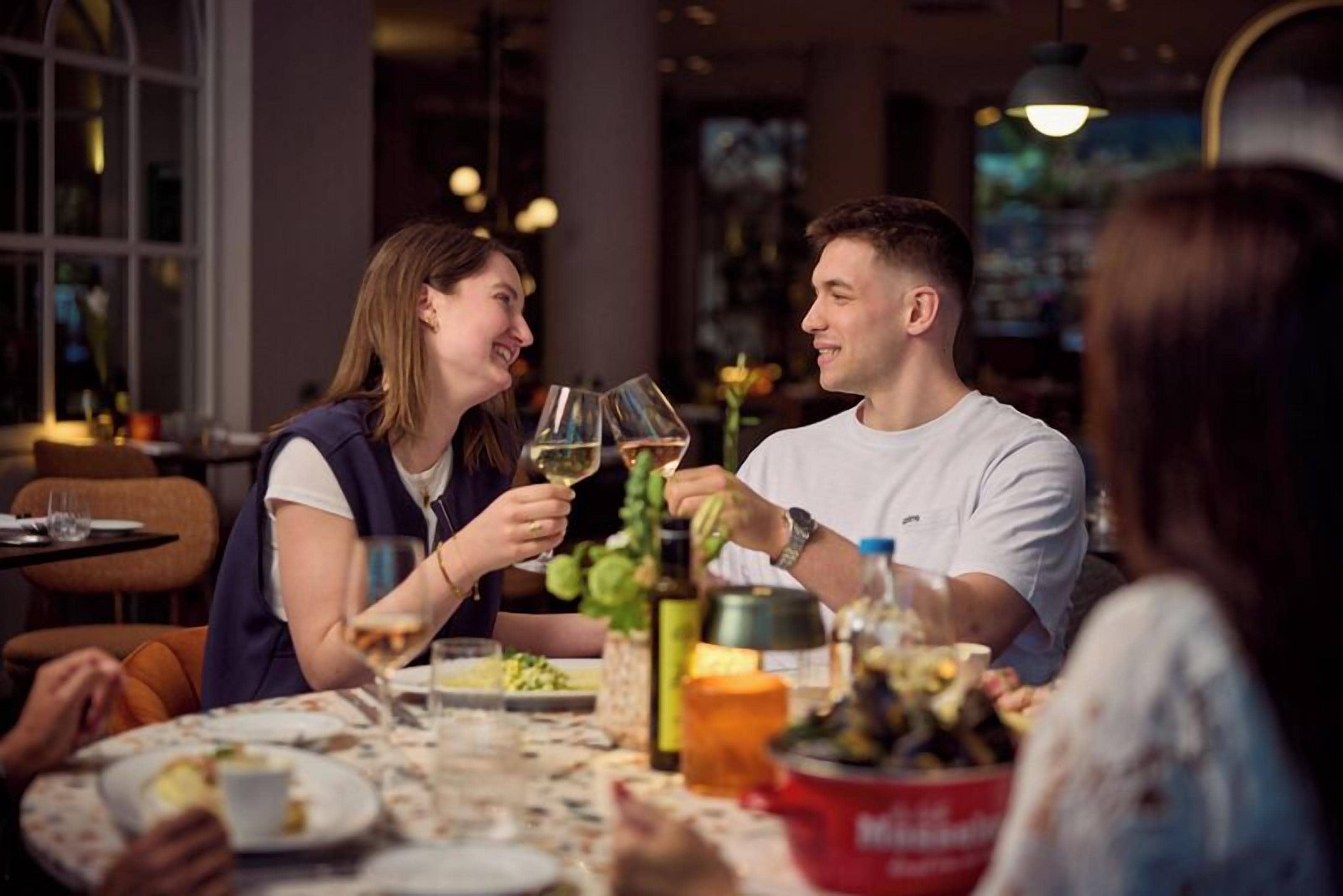 Un tavolo da pranzo con persone che brindano con bicchieri di vino, circondato da diversi piatti e un secchio rosso.