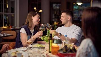 Un tavolo da pranzo con persone che brindano con bicchieri di vino, circondato da diversi piatti e un secchio rosso.