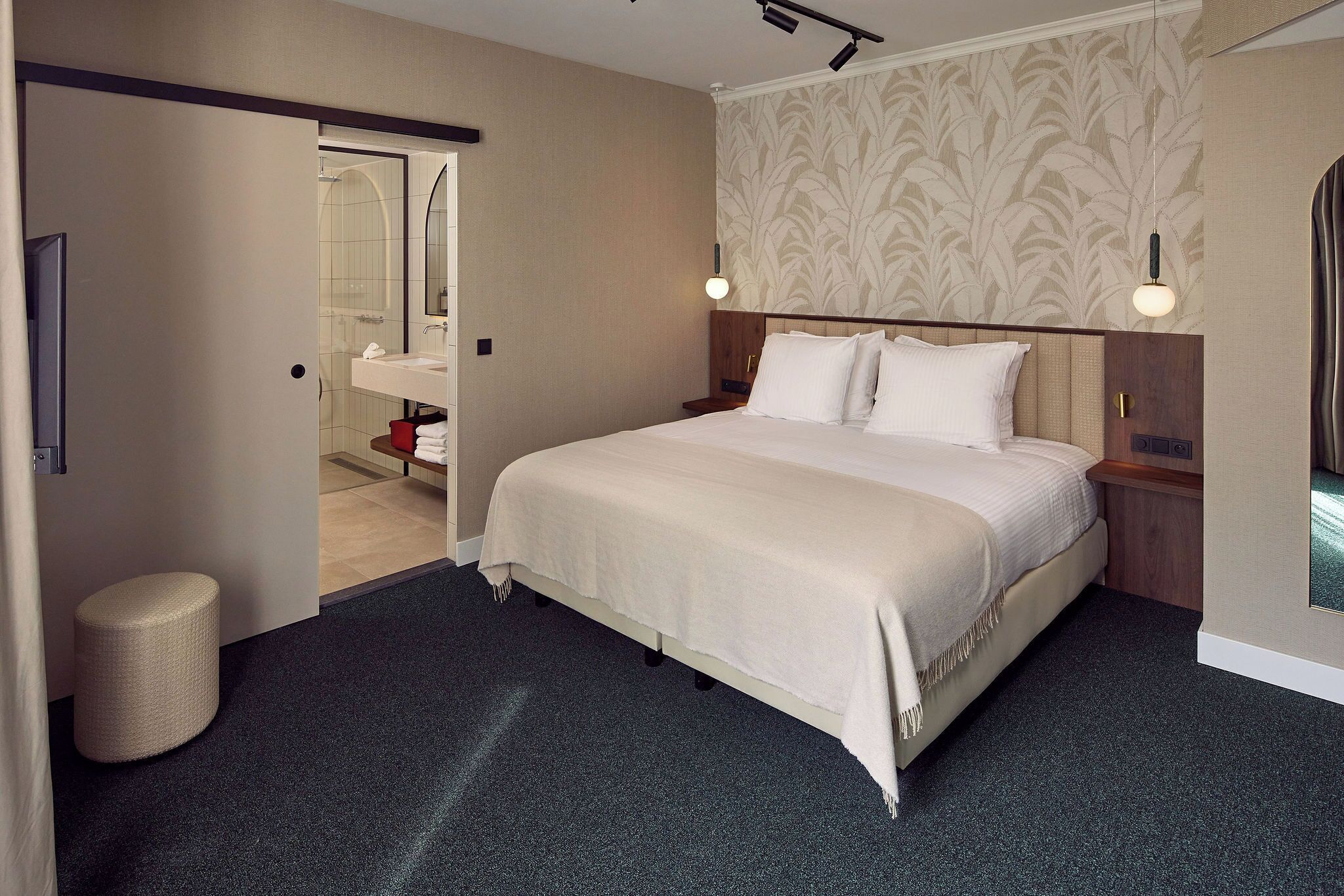 Habitación de hotel con una cama grande, una mesita de noche, un espejo y un baño visible a través de una puerta abierta.