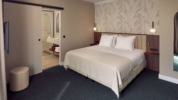 Habitación de hotel con una cama grande, una mesita de noche, un espejo y un baño visible a través de una puerta abierta.