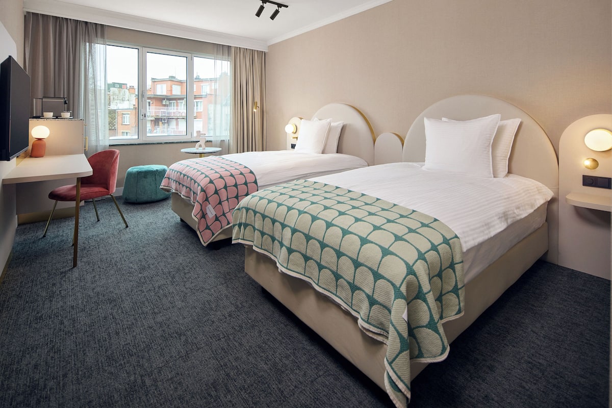 Une chambre d’hôtel avec deux lits, un bureau, une chaise et une télévision.