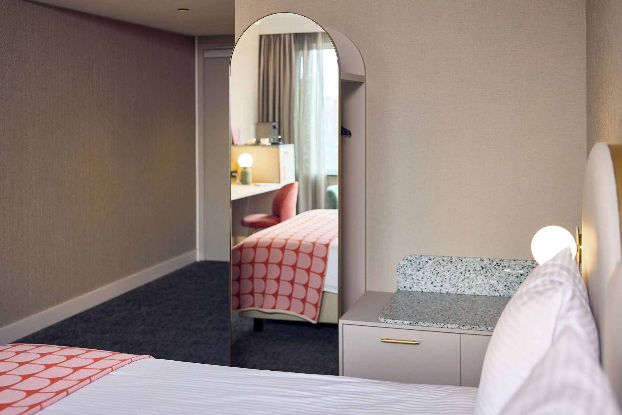 A hotel room with a bed, a desk, and a mirror.