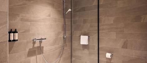 Un baño moderno con ducha de vidrio, inodoro y repisa con artículos de aseo.
