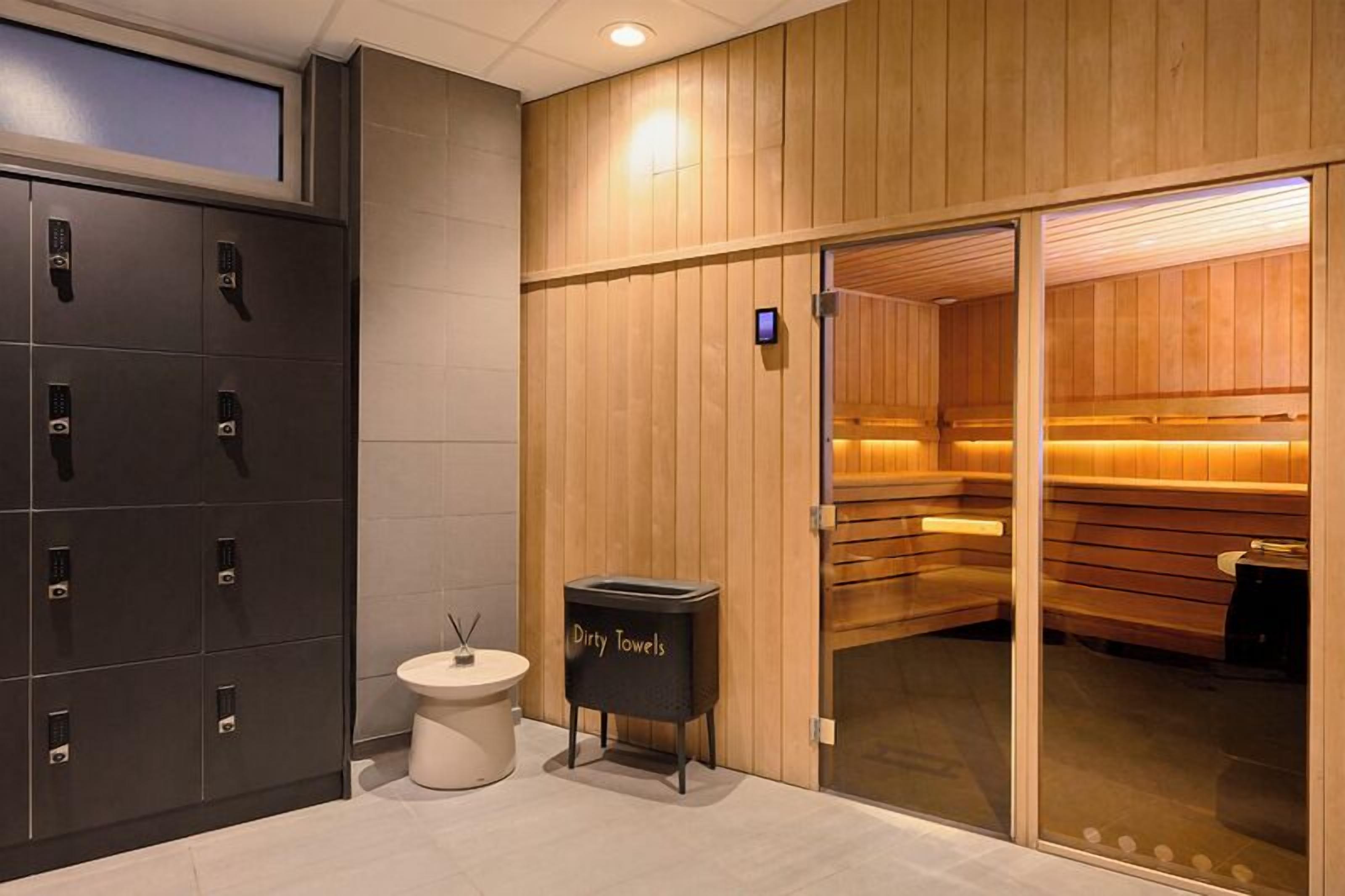 A sauna area with wooden walls and benches, a towel dispenser, and a storage cabinet with lockers.
