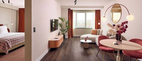 Ein modernes Hotelzimmer mit einem Bett, einer Couch, einem Esstisch und einem großen Fenster.
