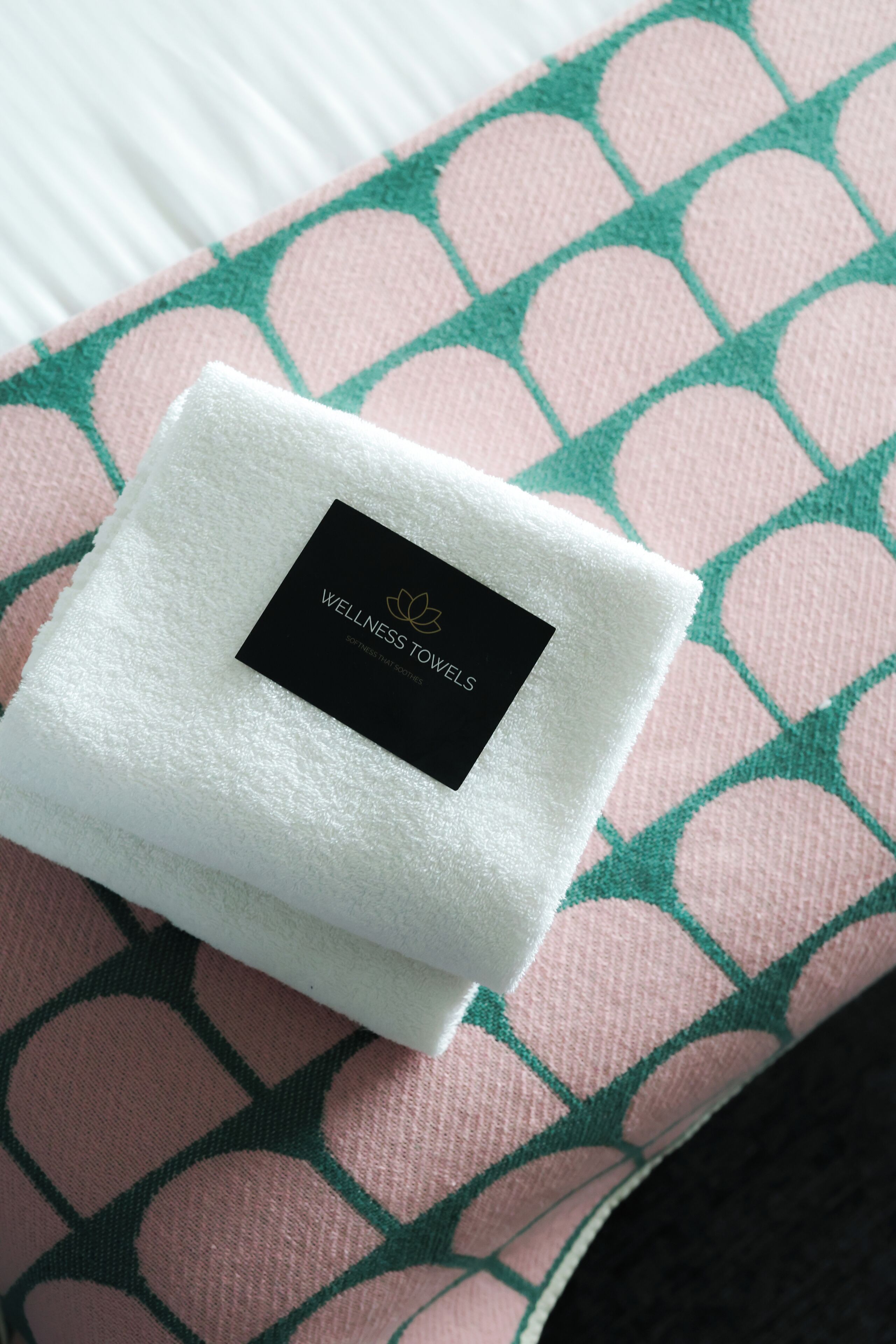 A folded white towel with a black label on a patterned pillow.