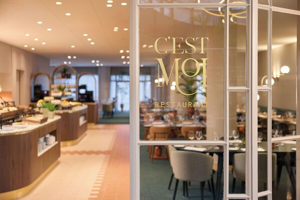 Interior de restaurante con zona de bufé, mesas de comedor y un muro de cristal que muestra el nombre del restaurante.