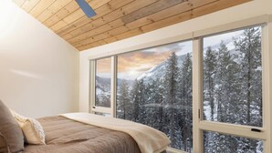 Een slaapkamer met een groot raam dat uitzicht geeft op een besneeuwde bossen en bergen.