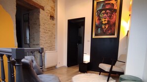 A living room with a stone wall, a black chair, a white rug, and a painting on the wall. - Stone house with swimming pool, in the heart of the vineyards of Nuits Saint Georges (Meuilley)