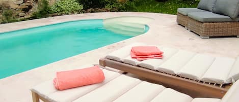 A poolside area with lounge chairs and a stone wall in the background.
