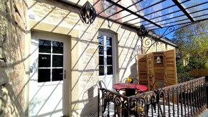 A covered patio with a tiled floor, a wooden table with chairs, and a metal railing. - Stone house with swimming pool, in the heart of the vineyards of Nuits Saint Georges (Meuilley)