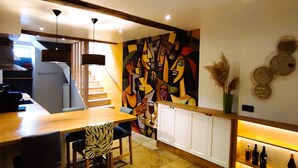 A modern kitchen with a dining area, featuring a staircase, a colorful abstract painting, and a wine display. - Stone house with swimming pool, in the heart of the vineyards of Nuits Saint Georges (Meuilley)