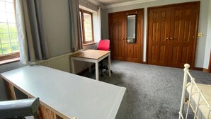 Una habitación con una mesa grande, una silla roja, una cama y puertas de madera dobles.