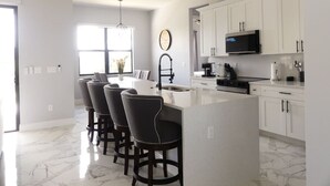 Una cocina moderna con armarios blancos, una isla central y taburetes de bar.