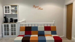 Ein Zimmer mit einem farbenfrohen Sofa, einem weißen Schrank mit Glastüren und einer Holztür.