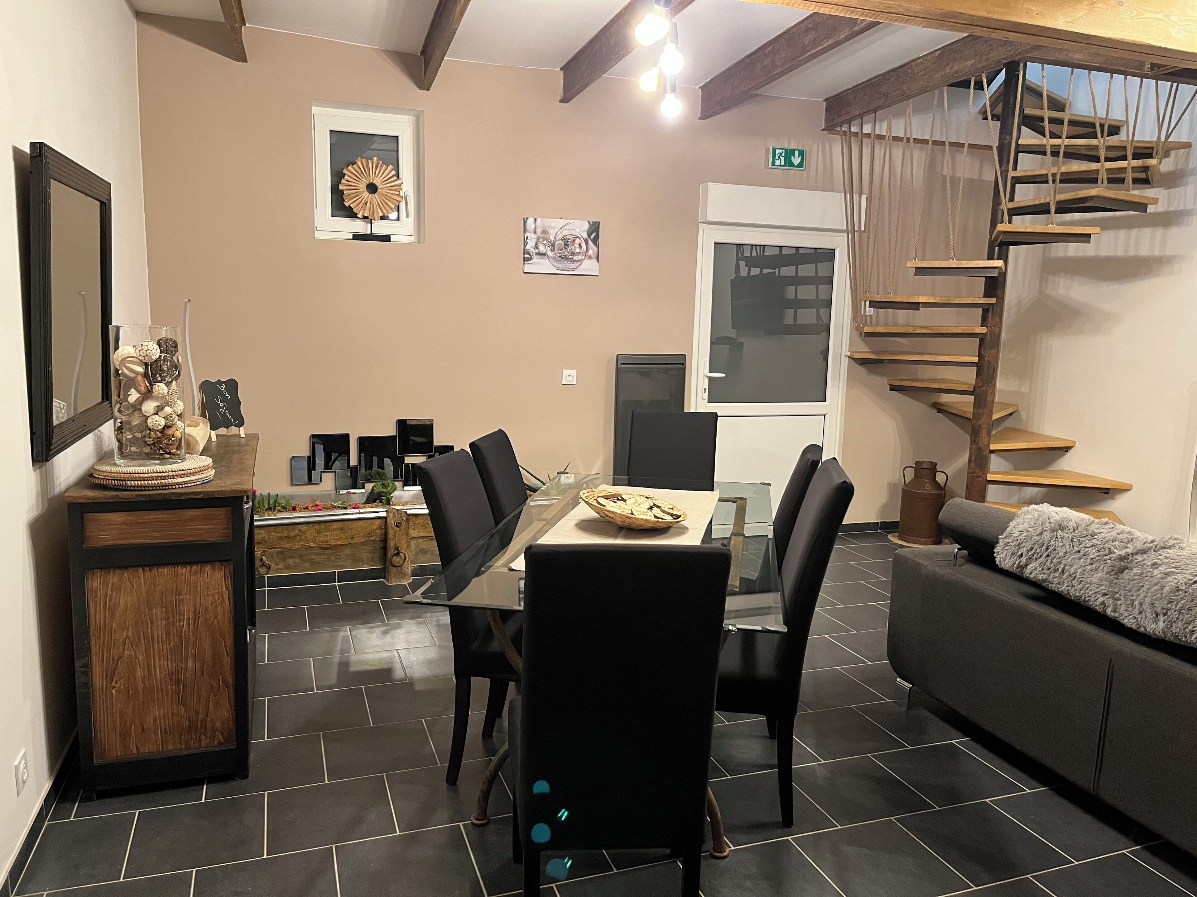 A dining area with a table and chairs, a sofa, a staircase, and a wall-mounted shelf.