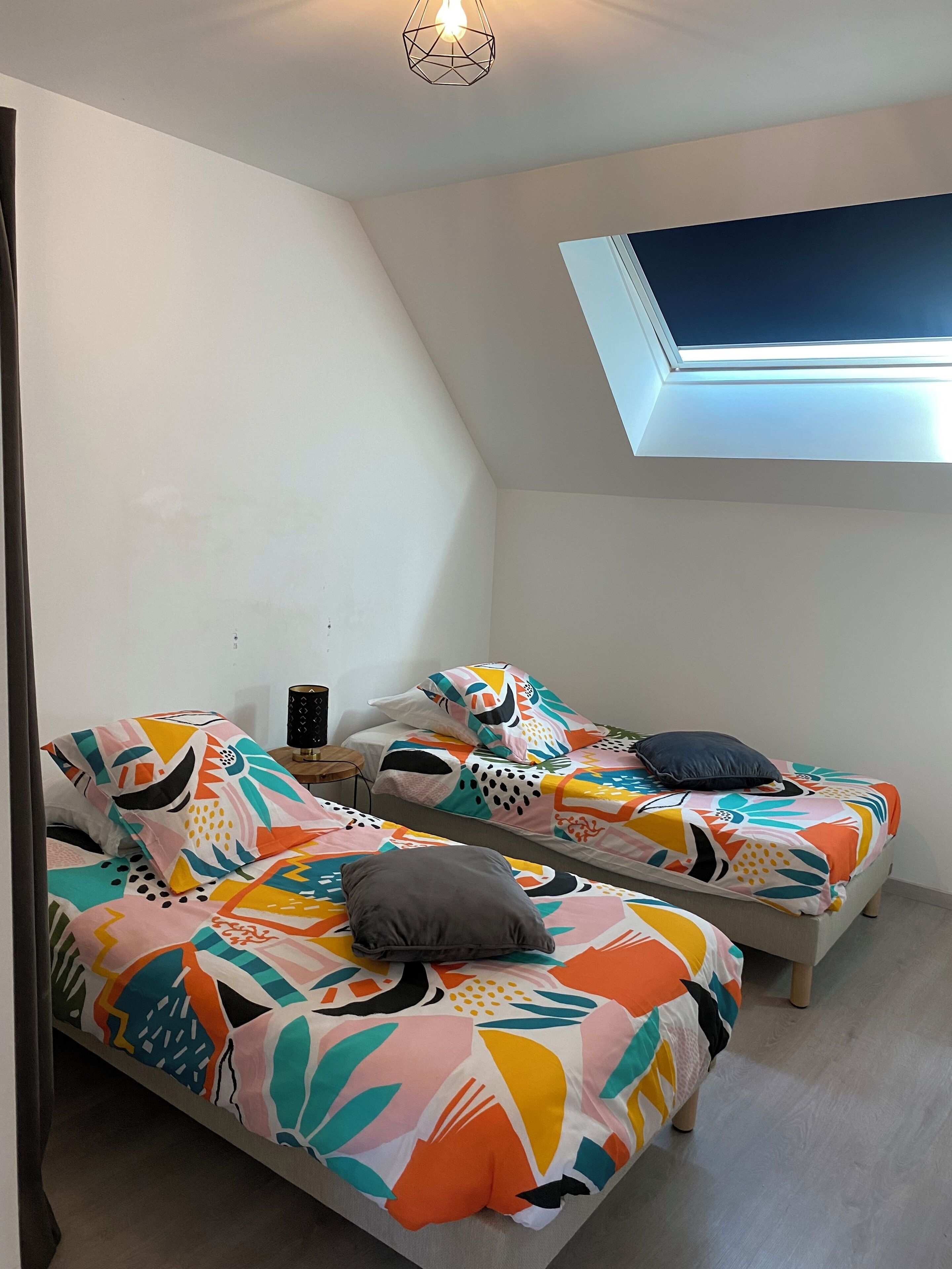 Un dormitorio con dos camas, un tragaluz y una mesita con lámpara.