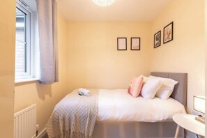 A bedroom with a bed, a bedside table, a window with curtains, and framed pictures on the wall.