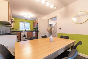A dining area with a wooden table, black chairs, and a vase of dried plants. - Host & Stay | Moresby Way (Peterborough)