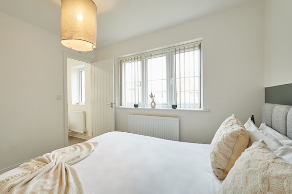 Une chambre avec un lit, un radiateur, une fenêtre avec des stores et un luminaire suspendu.