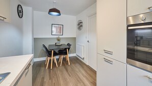 Une cuisine compacte avec un coin repas, comprenant une cuisinière moderne, une horloge et un luminaire suspendu.