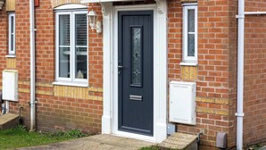 A brick house with a dark front door, white-framed windows, and a small porch. - Host & Stay | Bluebell Close (Corby)