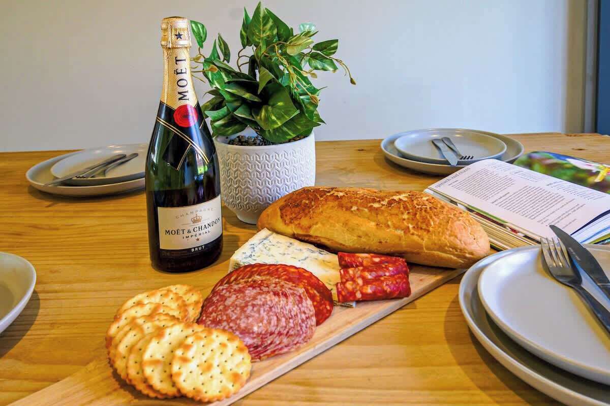 A table with a bottle of Moët & Chandon champagne, a loaf of bread, various cheeses, and cured meats.