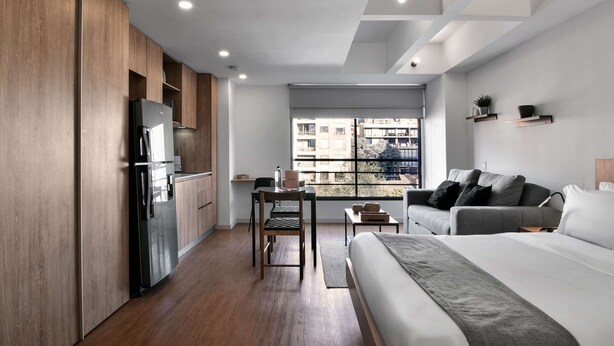Een moderne hotelkamer met een kitchenette, een bed, een bank en uitzicht op de stad.