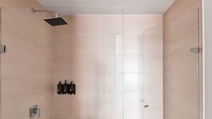 Een moderne douche met een handdouche, een zeepdispenser aan de muur en een bedieningspaneel.