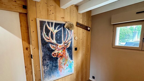 Een kamer met houten wanden, een groot schilderij van een hert en een bed, met uitzicht vanuit het raam.
