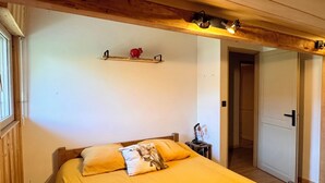 Een kamer met een bed, houten balken, een plankje met decoratie en een deur naar een andere kamer.