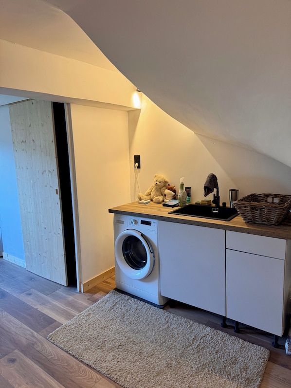 A compact laundry room with a washing machine, a sink, and a small countertop with various items.