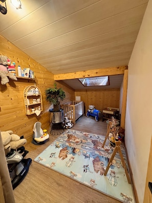 A cozy room with wooden walls, a crib, a play area with toys, and a window.