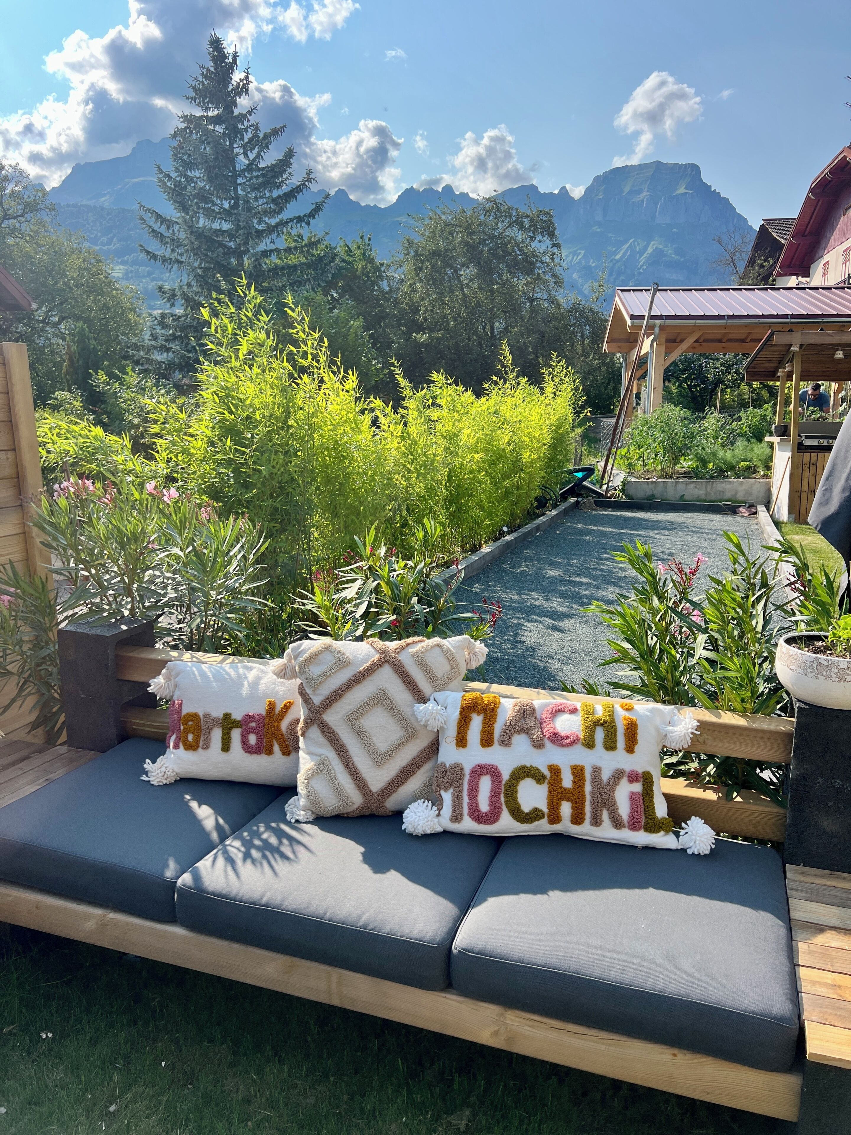 Un jardin avec un banc en bois, des plantes en pot et une vue sur les montagnes.